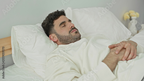 Foto Man lying on bed with hands clasped on stomach and eyes closed, pillow and wooden headboard visible in a bedroom; restless sleep