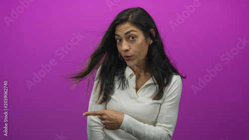 Tableau sur toile Woman pointing finger to left in studio with magenta wall and windblown hair; surprise playful curiosity