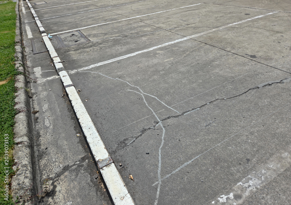 Fototapeta premium High Angle View of Empty Cracked Concrete Parking Lot Spaces with White Painted Lines and Curb