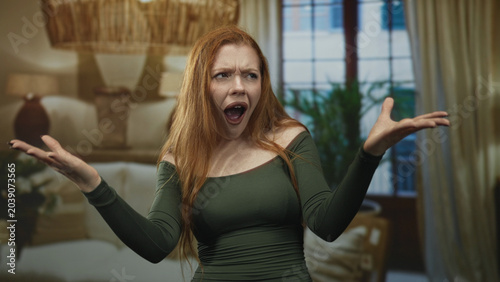 Fotografía Woman raising hands with open mouth shouting in building interior living room; frustration disbelief