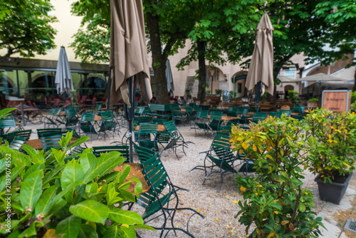Green metal chairs and closed umbrellas in a leafy spring courtyard cafe in Salzburg, Austria.