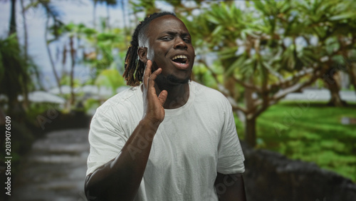 Schilderij op canvas Man points finger toward camera on a green park walkway wearing white tshirt, hand extended with visible palm and skeptical frown; skepticism