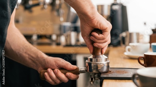 Barista holding a portafilter and using a metal tamper to press ground coffee for espresso