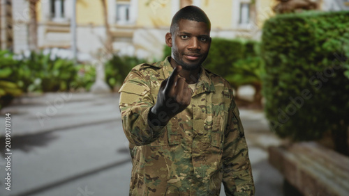 Schilderij op canvas Man soldier in camouflage uniform points index finger directly at camera while standing outside by a building entrance, commanding posture; duty resolve