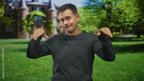 Billede på lærred Man with moustache raises hands palms outward in front of a grand building, giving a rueful shrug; indifference