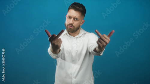 Photos Man in white shirt extends hands and shows middle fingers toward camera in studio; defiance provocation