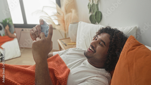 Foto Man holds smartphone with hand, smiling while lying on bed in building; contentment relaxation leisure morning