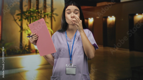 Fotografie Woman holds pink clipboard and makes ok gesture with hand in hospital lobby; confidence reassurance care