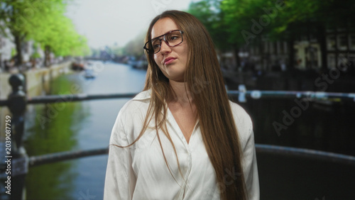 Foto Woman wearing glasses and white shirt with long hair, smirking and looking sideways on a street; confidence