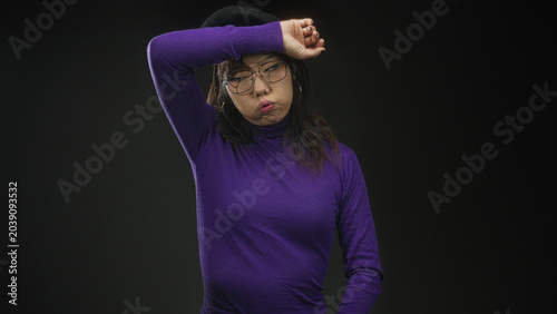 Photography Woman wearing beret and glasses shields forehead with arm while closing eyes and pouting in studio; fatigue introspection