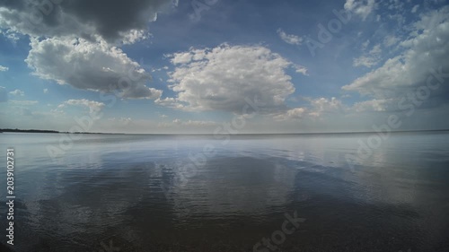 White cumulus clouds reflecting in a large calm lake with small wave distorting the clouds
