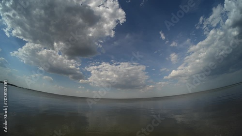 Fish-eye view of a large northern lake with cumulus clouds scatterd across a blue summer sky
