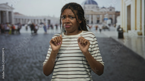 Photos Woman holding hands up near chest with fingers curled and a visible grimace in front of building; disgust discomfort