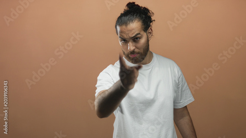 Foto Man in white t shirt pointing finger at camera with stern expression in studio against peach wall; accusation anger