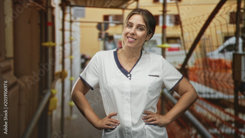 Tableau sur toile Woman nurse in white uniform with hands on hips smiling on street by scaffolding and orange safety fence; confidence care