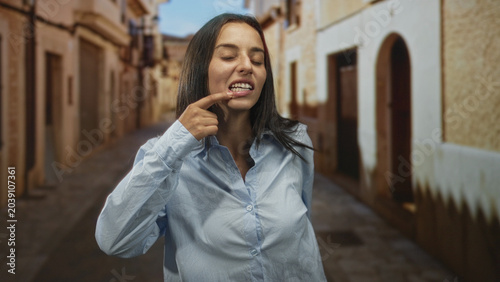 Foto Woman pulls cheeks with fingers and sticks tongue out on a street in an old town; playful mischief moment