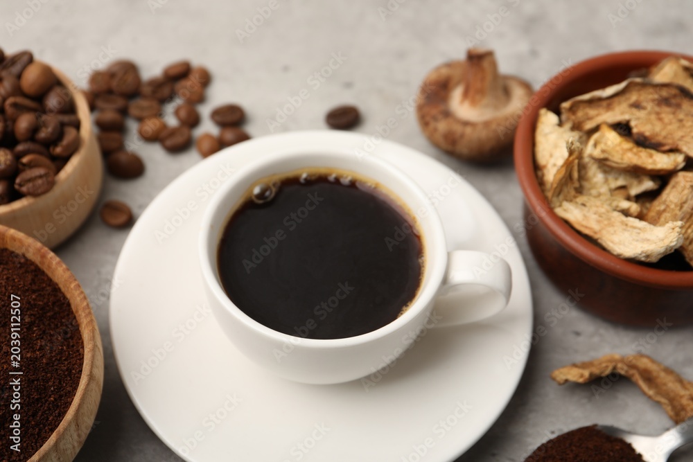 Obraz premium Cup of coffee, beans, powder and mushrooms on light grey table, closeup