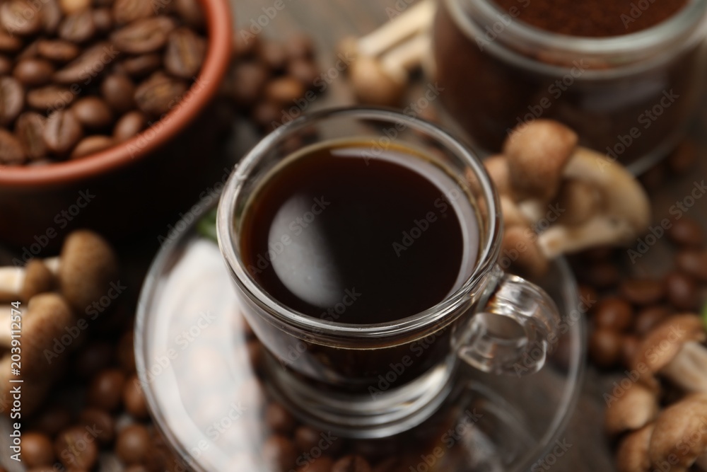 Fototapeta premium Cup of coffee, beans and mushrooms on wooden table, closeup