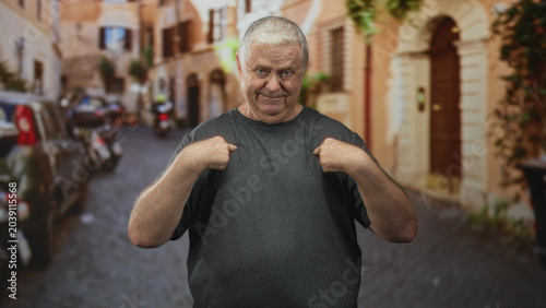 Tableau sur toile Man points both index fingers to chest in a narrow cobblestone street with parked cars and doorway, making an accusatory gesture toward himself; defiance self assertion