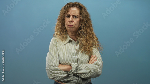Schilderij op canvas Woman with crossed arms and visible hands frowning in a studio portrait with blue backdrop; displeasure sternness