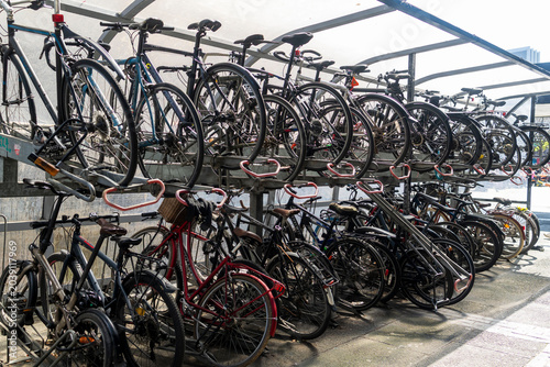 London, UK, 3 May 2026,  Two-tier metal bicycle rack filled with numerous parked bikes under a transparent shelter structure.