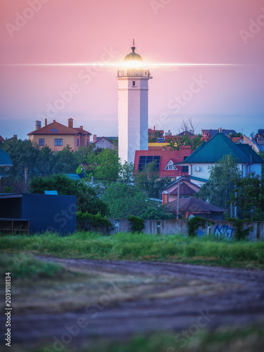 portrait view to lighthouse with signal light in village on sea shore in twilight
