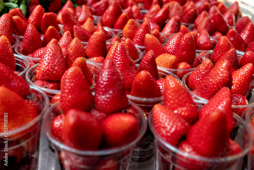 A closeup selective focus repetition pattern of fresh ripe red strawberries packed in clear plastic cups ready for sale at a market.
