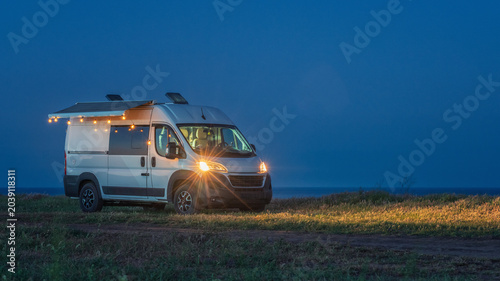 panoramic view to white camper van with romantic light in blue hour on the sea coast
