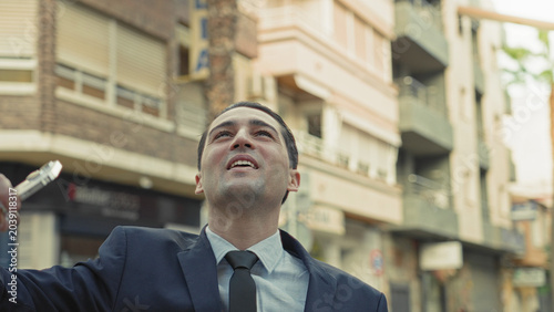 Billede på lærred Man in suit raises smartphone aloft on street, holding phone above head while gazing upward; confidence ambition drive