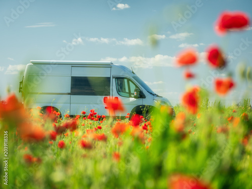 close up view to white van through red poppies in summer day