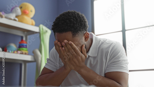 Photos Man smiling and clapping hands beside plush duck and toy shelf in a building room, briefly covering his face in playful peekaboo; gentle joy