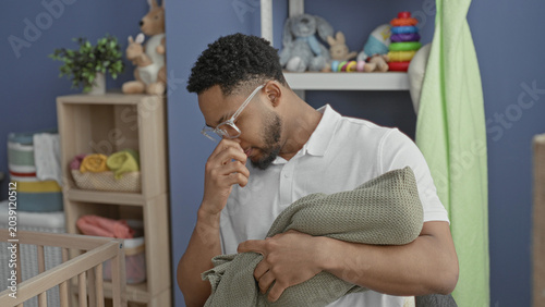 Фотография Man cradling wrapped baby in green blanket while touching nose in nursery building; new father bonding tired