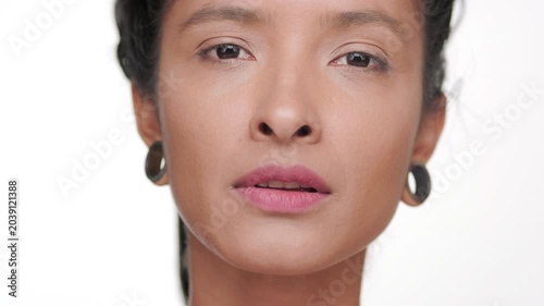 Big close-up shot of hispanic woman with bronzed skin strokes her jawline presenting revitalized skin on light background | Beauty ad concept