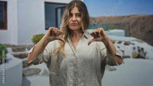 фотографія Woman giving thumbs down gesture in white building courtyard, hands raised at chest level; disapproval critique