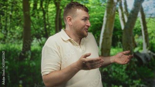 Man shrugging with open palms in a forest with birch trees and green foliage nearby; surprise questioning.