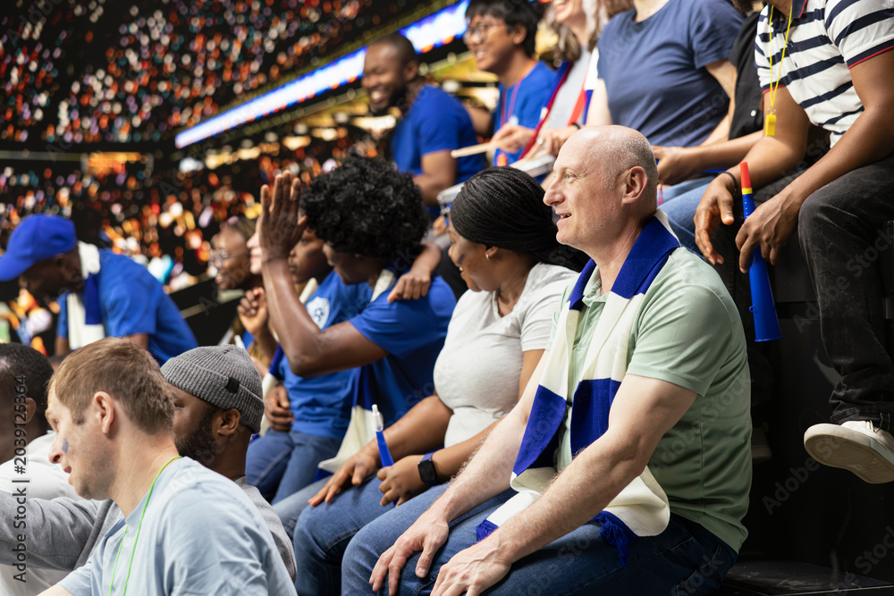 Fototapeta premium Black father spending quality weekend time with son at packed soccer stadium full of cheering fans. Football family lifestyle, parenthood and family bonding, blue team support and childhood joy.