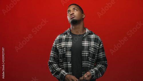 Photos Man holds wrench in studio with visible hand and apathetic facial gesture, plaid shirt against red backdrop; quiet contemplation
