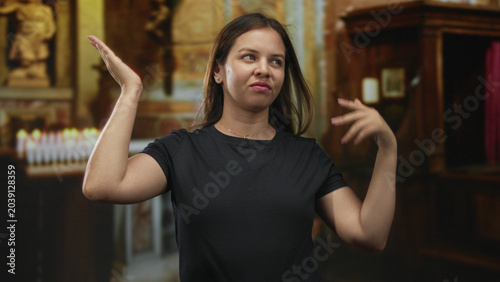 Tableau sur toile Young woman shrugging with hands raised palms up near votive candles in church building; indifference doubt