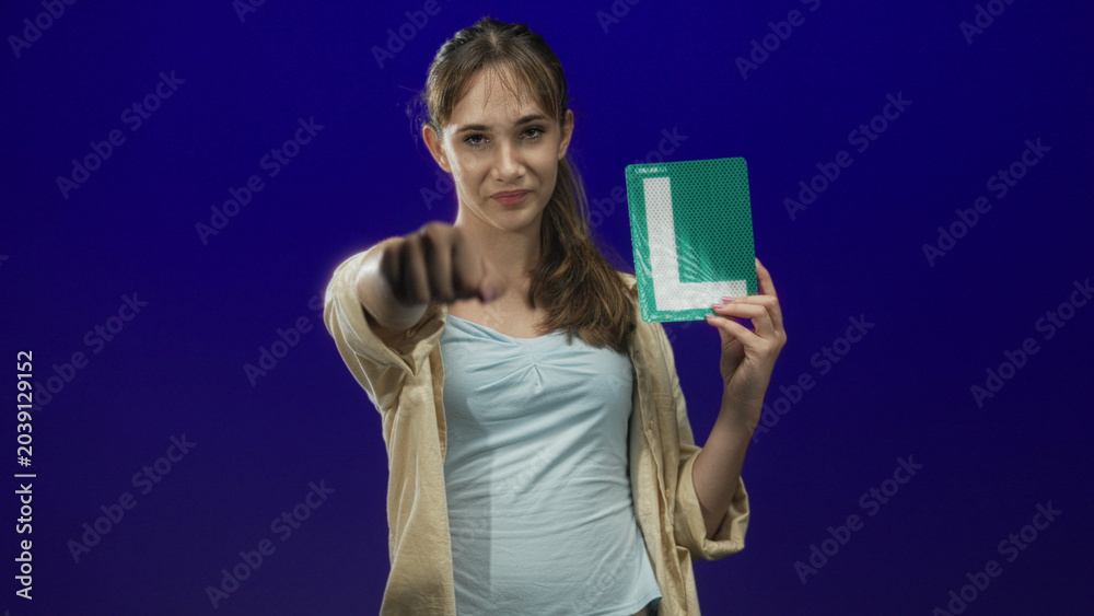 Fototapeta premium Woman holding a learner plate with a fist pump gesture in studio with a purple backdrop; new license confidence.