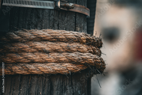 фотографія Thick natural rope tightly bound around a weathered wooden post with metal clamp