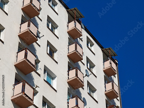 Old apartment building facade with rows of small balconies, windows and satellite dishes against clear blue sky, Eastern European block of flats renovation and real estate concept, no people