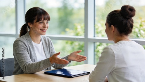 Friendly female job candidate smiling and gesturing during an interview with a recruiter in a bright modern office, discussing career opportunities, employment, and professional