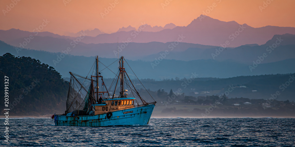 Obraz premium Fishing Trawler in Ocean with Mountain Backdrop at Sunset