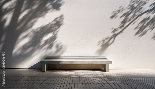 minimalist concrete bench with strong tree shadows on a white wall and floor creating a stark outdoor architectural scene