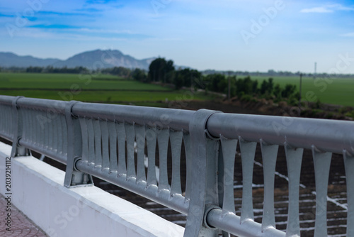 Sturdy gray metal bridge railing overlooking a beautiful green rice field and distant mountains