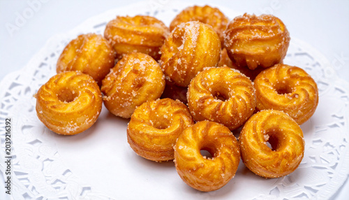 Mini Donuts Stacked: A delightful pile of golden-brown mini donuts, dusted with sugar and arranged on a white doily, offering a sweet temptation.