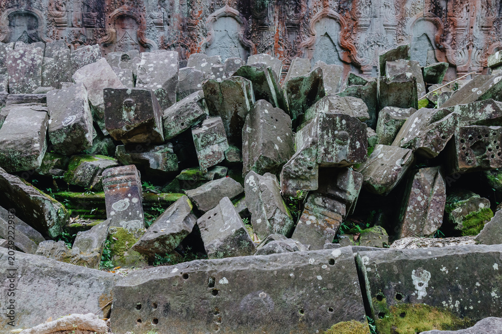 Naklejka premium Ancient moss-covered stone ruins overgrown with vegetation at Ta Prohm temple in Siem Reap, Cambodia. The jungle setting highlights the passage of time.