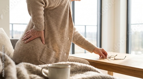 Elderly woman holding her painful lower back while sitting at home