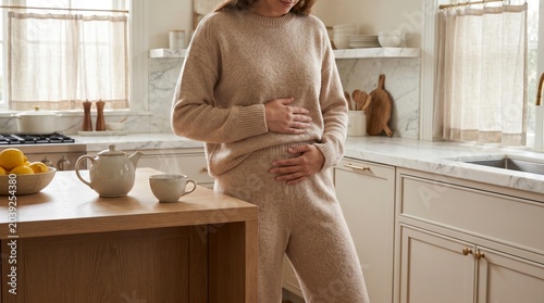 Pregnant woman holding her belly in a cozy home kitchen with tea