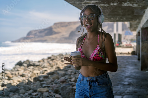 Фотография Young woman enjoying music and coffee on rocky ocean shore